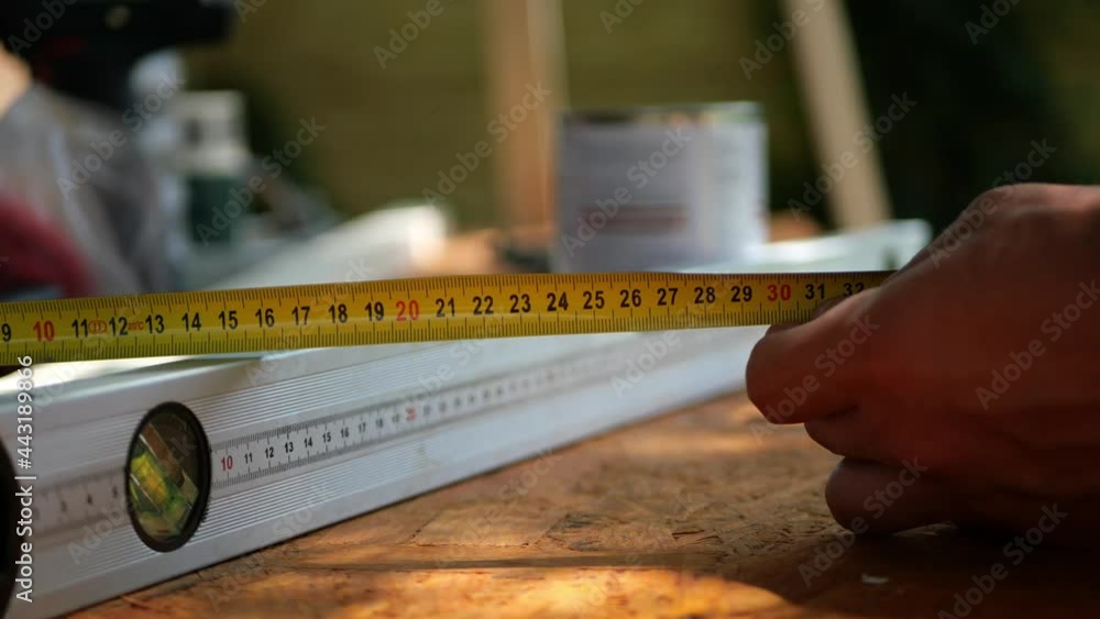 Man's hand holding tape measure above construction spirit bubble level tool, measuring the distance above plywood, close up Man's hand holding tape measure above construction spirit bubble level tool, measuring the distance above plywood, close up