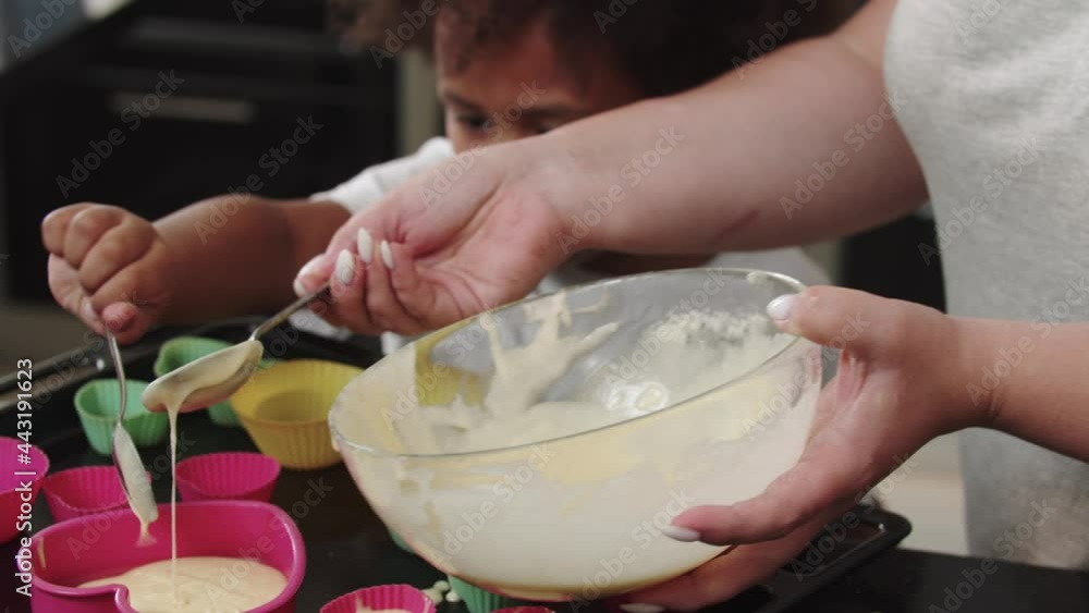 Mixed family pouring raw liquid dough in the cake moulds with a spoon Mixed family pouring raw liquid dough in the cake moulds with a spoon