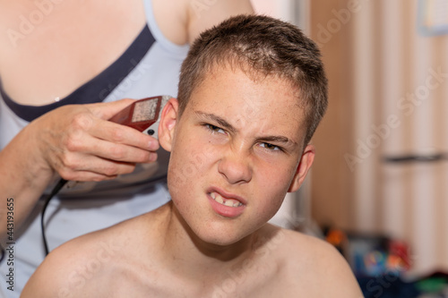 Cutting the hair of a boy, young guy at home due to the lockdown and quarantine coronavirus epidemic. Parents and relatives help each other get their hair without going to the hairdresser