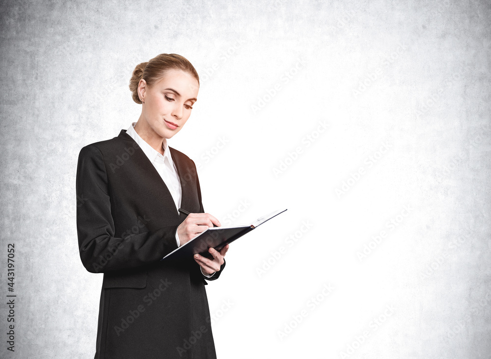 Attractive young businesswoman in suit holding a notebook and pondering how to optimize business process to boost sales of the company. Concrete wall on background Attractive young businesswoman in suit holding a notebook and pondering how to optimize business process to boost sales of the company. Concrete wall on background