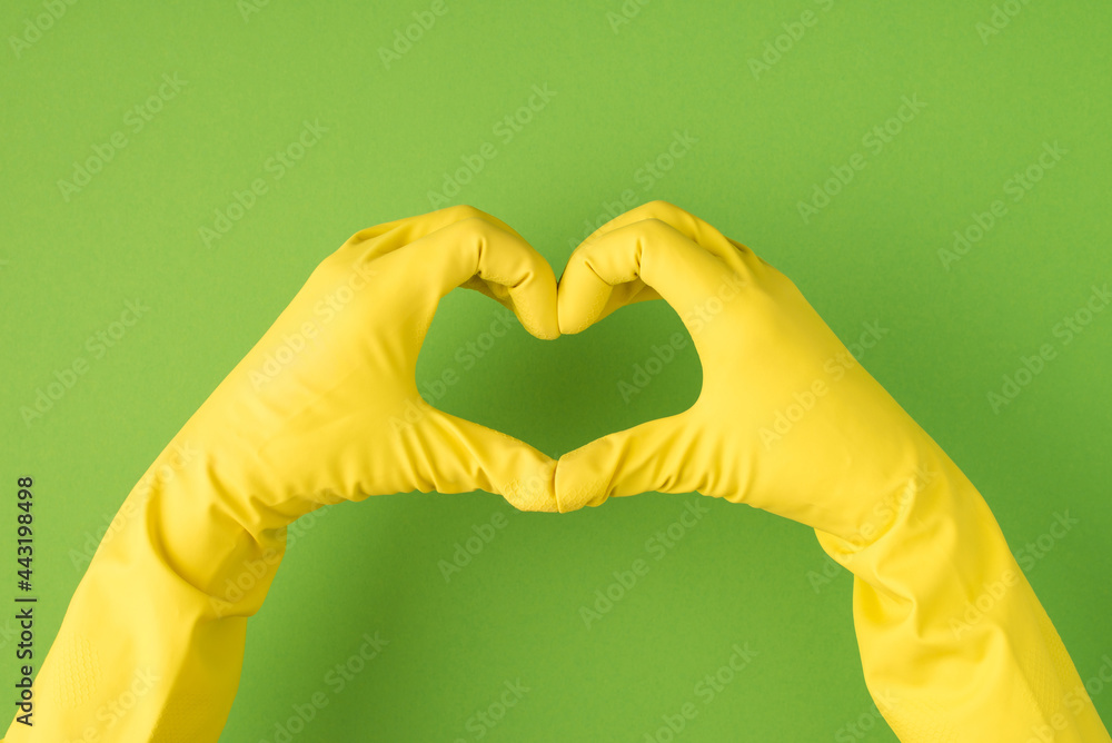 Obraz premium Above photo of hands in yellow gloves doing the gesture as heart isolated on the green background