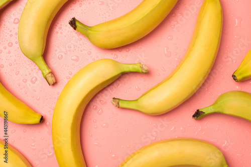 Top view photo of ripe yellow bananas and water drops on isolated pastel pink background
