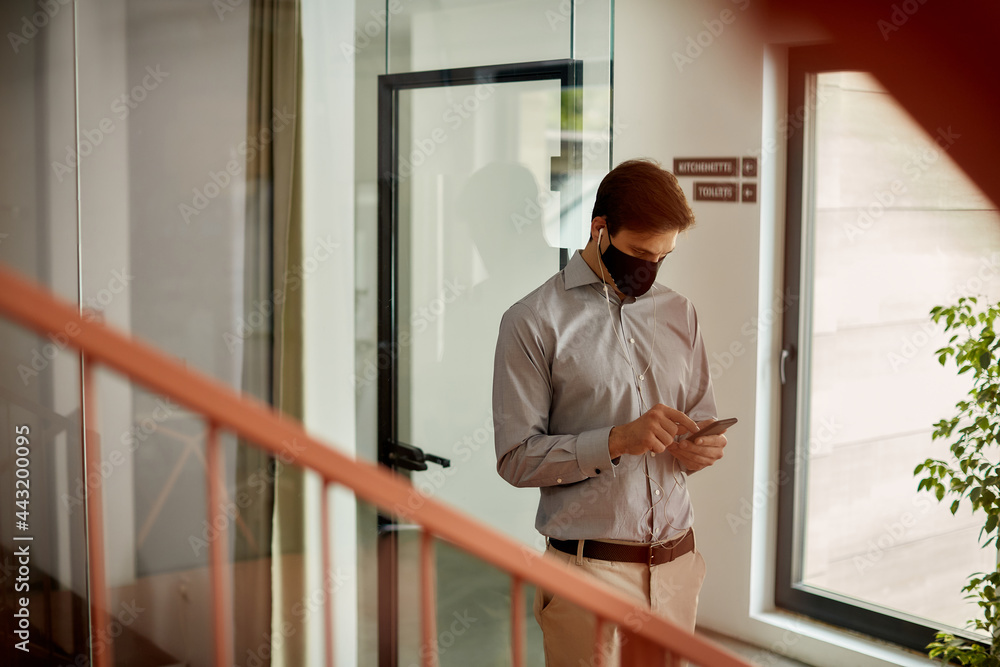 Businessman with protective face mask using mobile phone in a hallway. Businessman with protective face mask using mobile phone in a hallway.