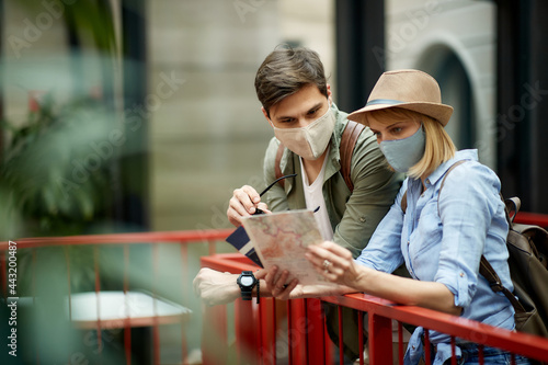 Happy tourist couple wearing protective face mask on their vacation and looking at the map.