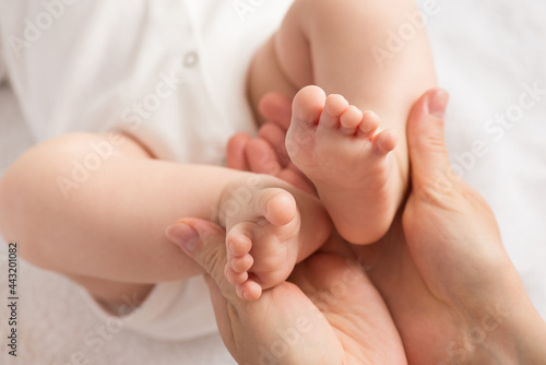 Closeup photo of mother's hands holding newborn's tiny feet on isolated white textile background © ActionGP