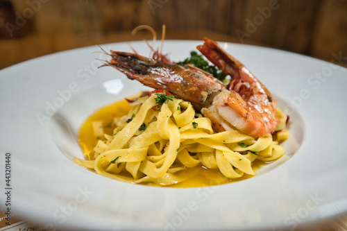Scampi, Riesengarnele auf Tagliatelle, Pasta mit einer Safransoße angerichtet auf einem weißen Teller