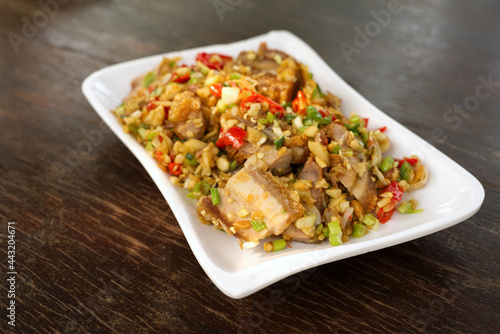 Stir Fried Crispy Pork with Fresh Chili in a white plate, put on a brown wooden dining table.