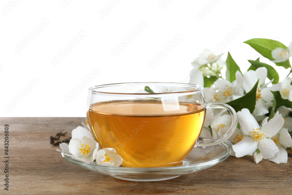 Glass cup of aromatic jasmine tea and fresh flowers on wooden table against white background