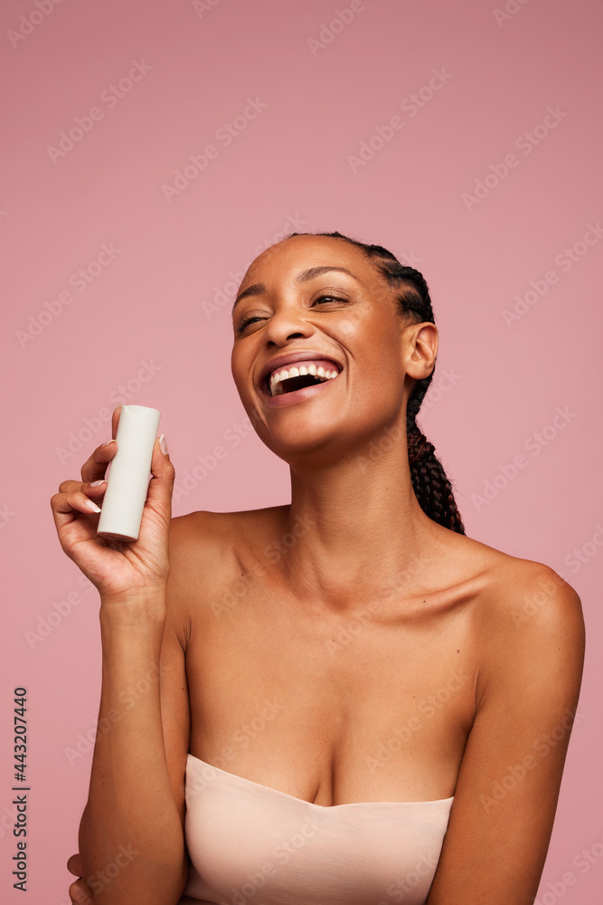 Woman holding a skincare product and smiling - obrazy, fototapety, plakaty 
