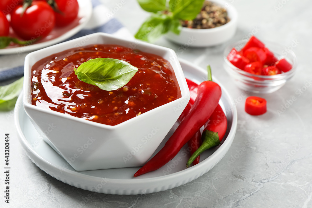 Spicy chili sauce with basil on light grey table Spicy chili sauce with basil on light grey table
