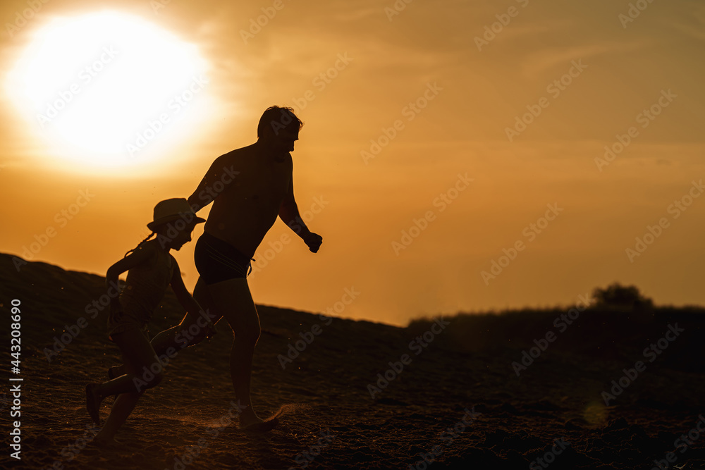 Happy family dad and daughter run from shore into water. Summer family vacation on the shore of a lake or river. a man and a girl jump into the water, splash at sunset. Silhouettes. Active recreation.