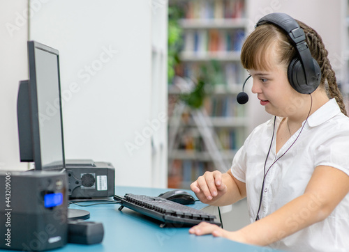 Young girl with syndrome down uses computer at home. Education for disabled children concept photo