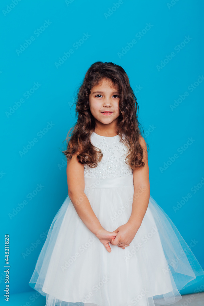 Beautiful little curly girl 5 years old in a white dress on a blue background