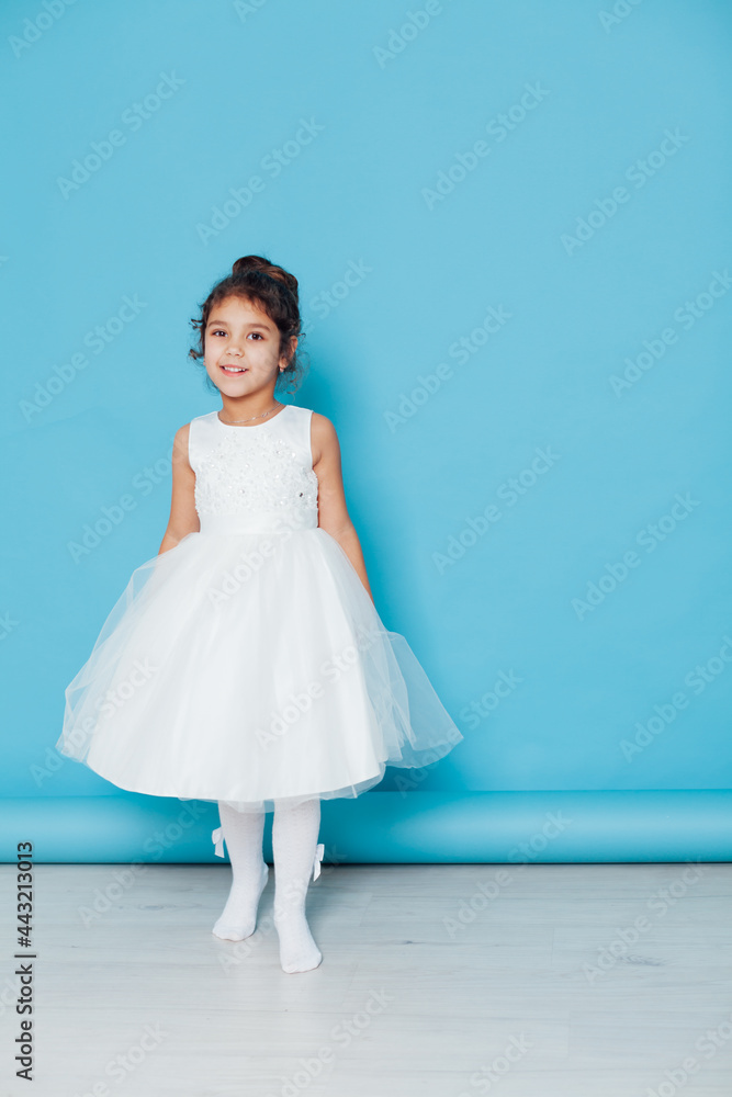 Beautiful little girl dances to the song in a white dress on a blue background Beautiful little girl dances to the song in a white dress on a blue background