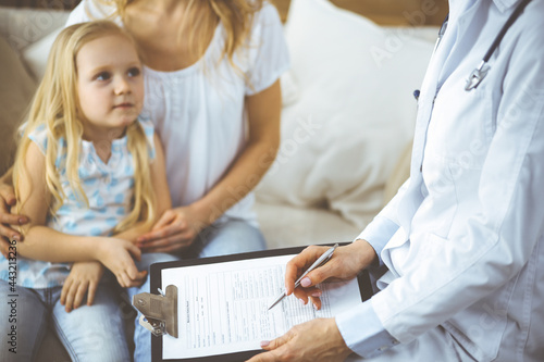 Doctor and patient. Pediatrician using clipboard while examining little girl with her mother in clinic at home. Happy cute caucasian child at medical exam. Medicine concept © rogerphoto
