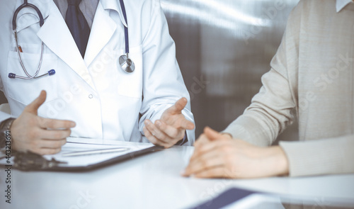 Unknown male doctor and patient woman discussing something while sitting in clinic. Best medical service in hospital  medicine  pandemic stop