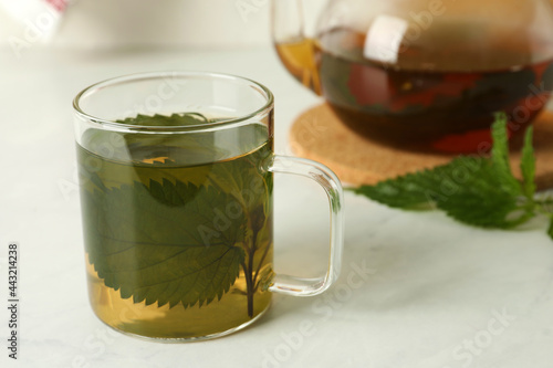 Glass cup of aromatic nettle tea on white table, space for text