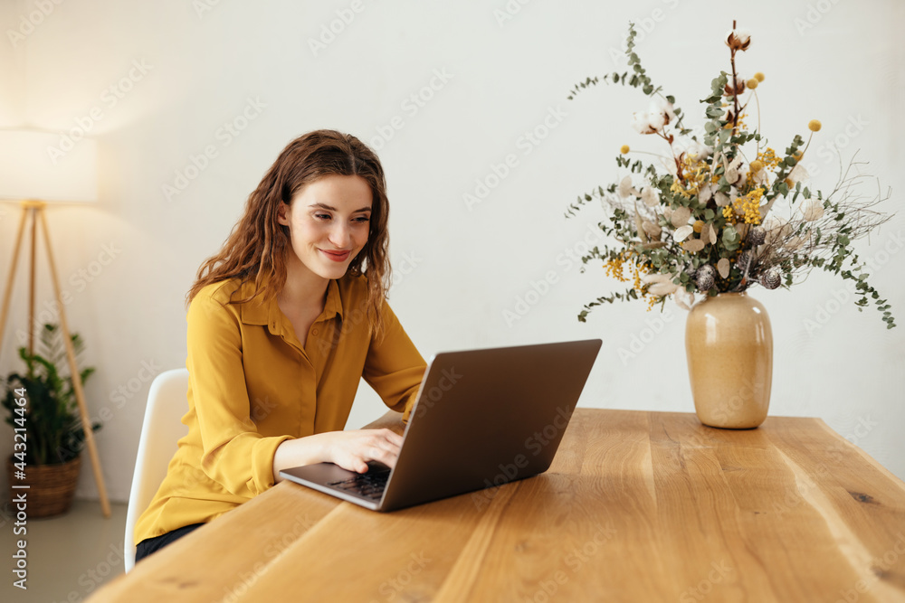 Young woman smiling happily to herself as she works on a laptop Young woman smiling happily to herself as she works on a laptop