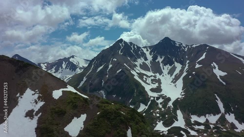 Aerial view of mountain chain on Kamchatka peninsula. Drone 4k footage, dramatic aerial view. Snowy mountains in July 2021. Clouds moving fast