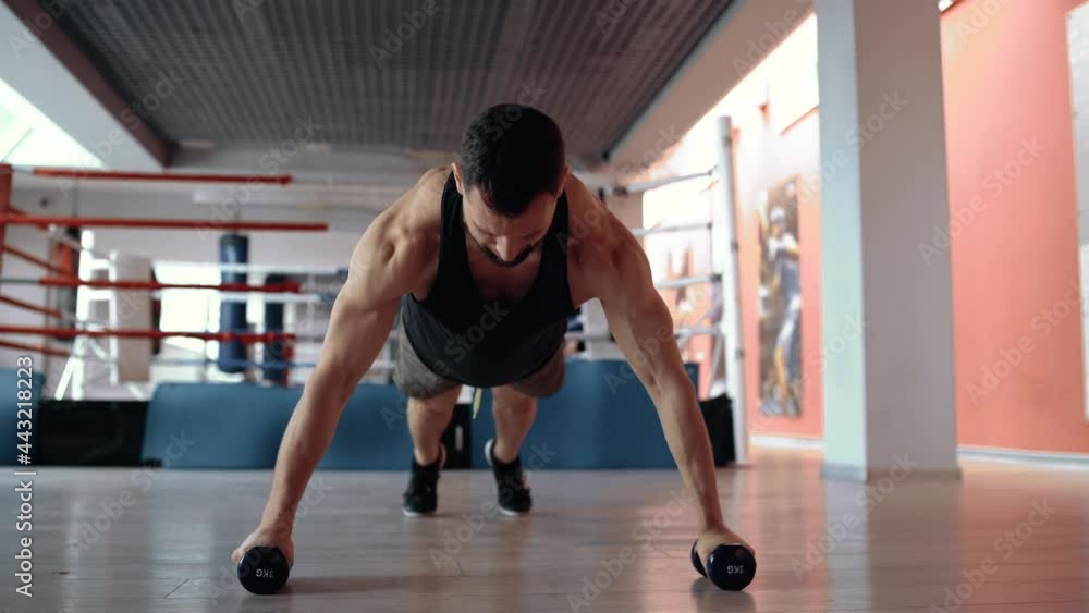 A trained, motivated man does push-ups with his hands on dumbbells in a gym. Healthy lifestyle. Sport concept A trained, motivated man does push-ups with his hands on dumbbells in a gym. Healthy lifestyle. Sport concept