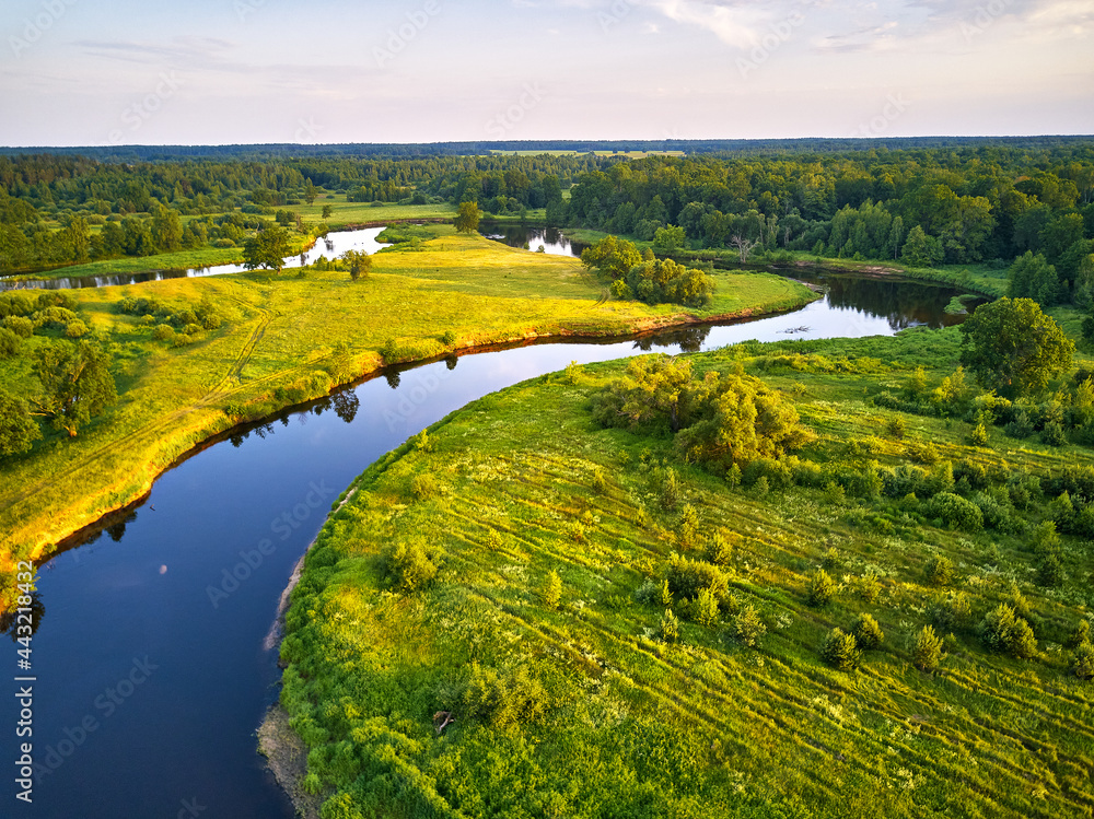 Aerial view of river in green meadows, beautiful sunset light. Meander evening panorama