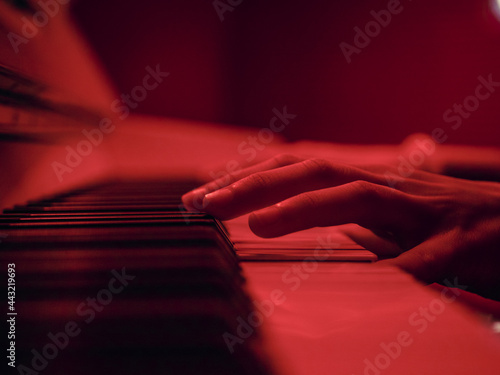 Wall Mural Close up shot of the hands of a young girl playing a piano in a dark red setting