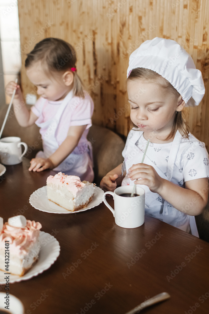 Children in the kitchen cook with their parents. Making homemade cake, pastries or cookies for the whole family. Happy childhood concept. Little twin sisters in kitchen aprons and chef hats Children in the kitchen cook with their parents. Making homemade cake, pastries or cookies for the whole family. Happy childhood concept. Little twin sisters in kitchen aprons and chef hats