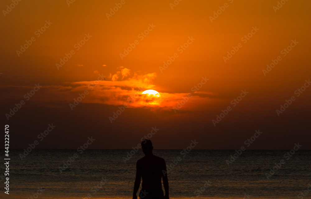 Silhouette of a man on the beach at sunrise. Boy watching the beautiful sunrise on the seashore. Summer vacation, holidays, travel, and people concept