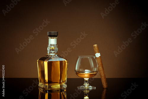 close up view of cigar, bottle of cognac and a glass aside on color back.  © Dmitry Ersler