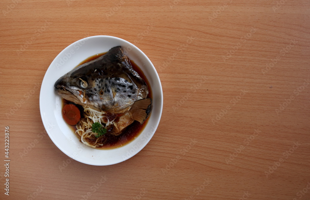 Boiled salmon head with soy sauce (Salmon kabutoni) on white round dish and brown wood background.