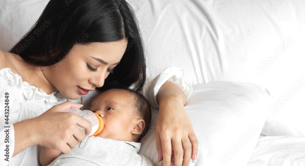 Portrait of enjoy happy love family asian mother playing with adorable little asian baby.Mom feeding bottle of milk to cute son in a white bedroom.Love of family concept Portrait of enjoy happy love family asian mother playing with adorable little asian baby.Mom feeding bottle of milk to cute son in a white bedroom.Love of family concept