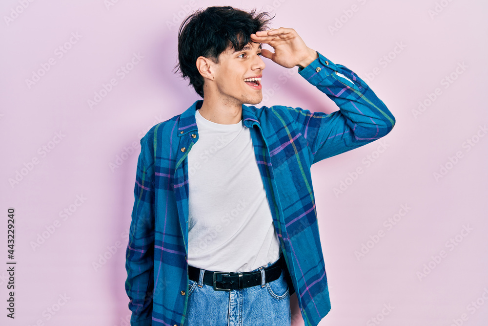 Handsome hipster young man wearing casual white t shirt and vintage shirt very happy and smiling looking far away with hand over head. searching concept. Handsome hipster young man wearing casual white t shirt and vintage shirt very happy and smiling looking far away with hand over head. searching concept.