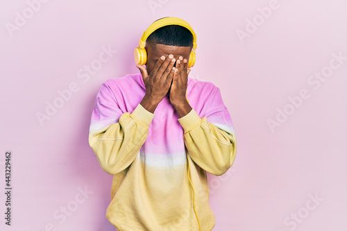 Young black man listening to music wearing headphones with sad expression covering face with hands while crying. depression concept.