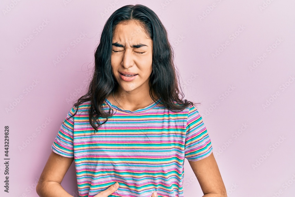 Hispanic teenager girl with dental braces wearing casual clothes with hand on stomach because nausea, painful disease feeling unwell. ache concept. Hispanic teenager girl with dental braces wearing casual clothes with hand on stomach because nausea, painful disease feeling unwell. ache concept.