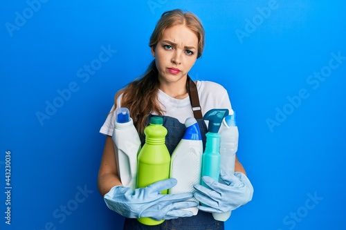 Beautiful blonde caucasian woman wearing cleaner apron holding cleaning products skeptic and nervous, frowning upset because of problem. negative person.