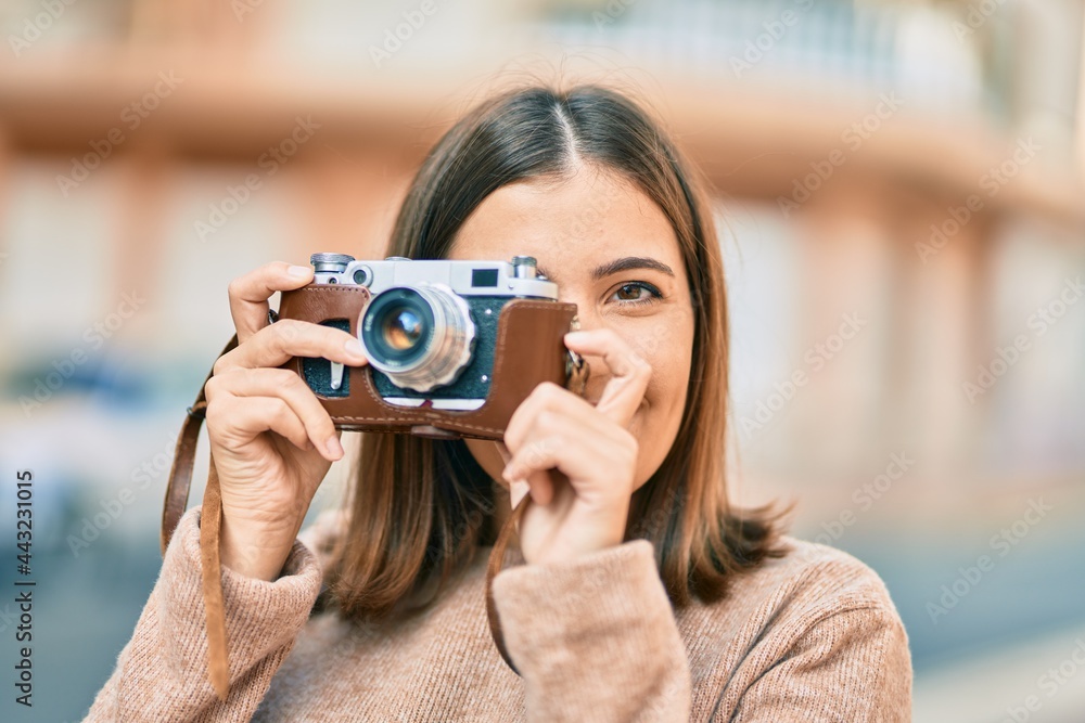Young hispanic tourist woman smiling happy using vintage camera at the city.