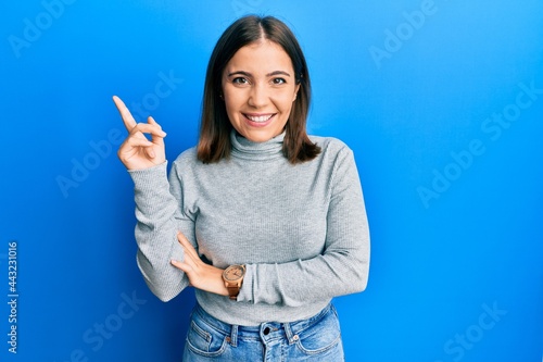 Young beautiful woman wearing casual turtleneck sweater smiling happy pointing with hand and finger to the side