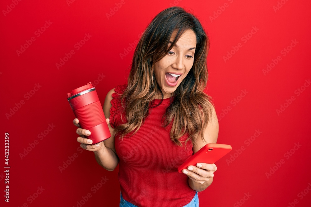 Young latin woman using smartphone and drinking a cup of coffee celebrating crazy and amazed for success with open eyes screaming excited. Young latin woman using smartphone and drinking a cup of coffee celebrating crazy and amazed for success with open eyes screaming excited.