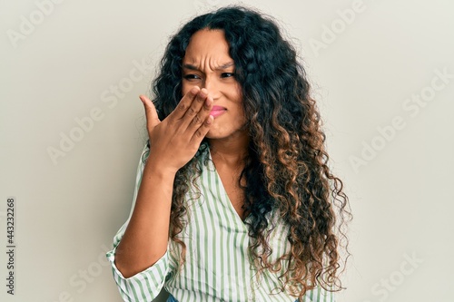 Young latin woman wearing casual clothes smelling something stinky and disgusting, intolerable smell, holding breath with fingers on nose. bad smell