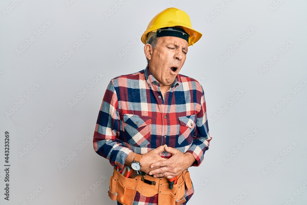 Senior hispanic man wearing handyman uniform with hand on stomach because indigestion, painful illness feeling unwell. ache concept. Senior hispanic man wearing handyman uniform with hand on stomach because indigestion, painful illness feeling unwell. ache concept.