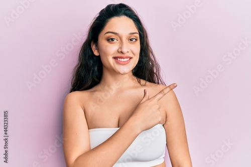 Beautiful middle eastern woman standing wearing a top showing skin smiling cheerful pointing with hand and finger up to the side