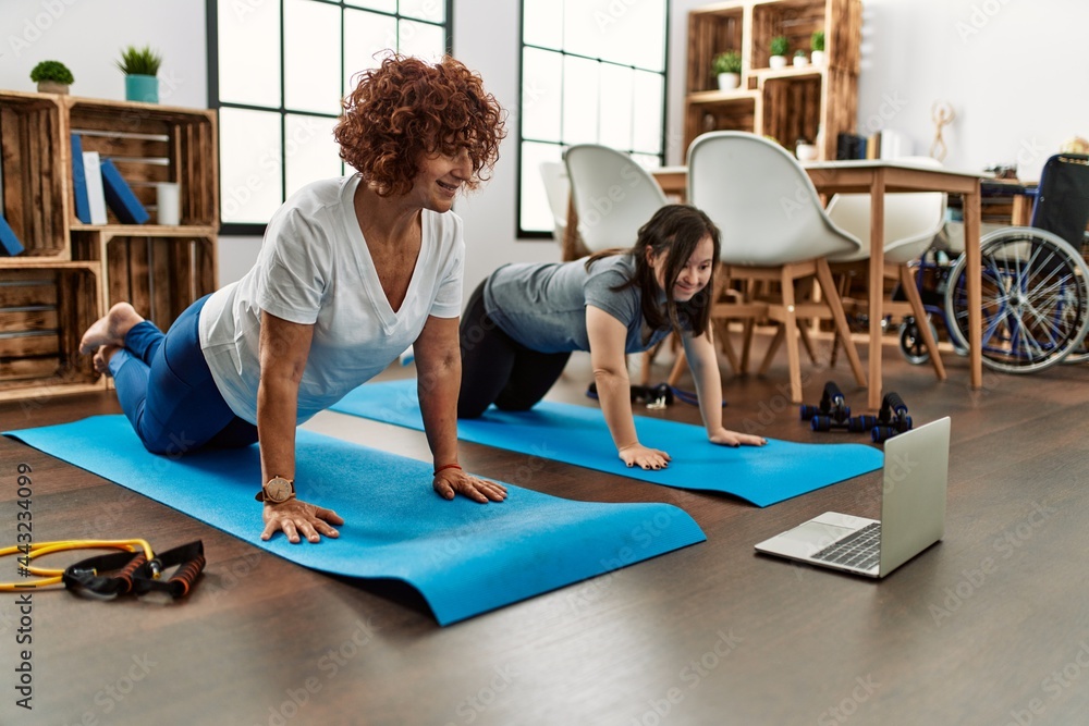 Mature mother and down syndrome daughter doing exercise at home. Stretching at the living room Mature mother and down syndrome daughter doing exercise at home. Stretching at the living room