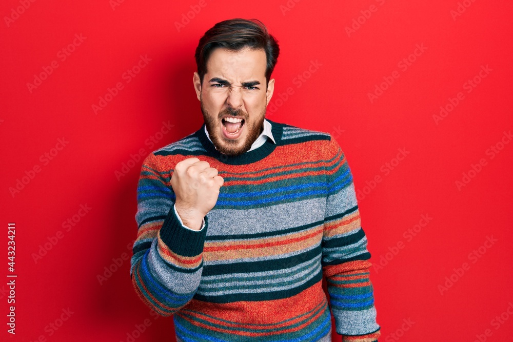 Handsome caucasian man with beard wearing elegant wool winter sweater angry and mad raising fist frustrated and furious while shouting with anger. rage and aggressive concept. Handsome caucasian man with beard wearing elegant wool winter sweater angry and mad raising fist frustrated and furious while shouting with anger. rage and aggressive concept.