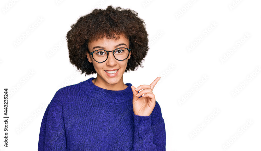 Young hispanic girl wearing casual winter sweater and glasses with a big smile on face, pointing with hand and finger to the side looking at the camera.