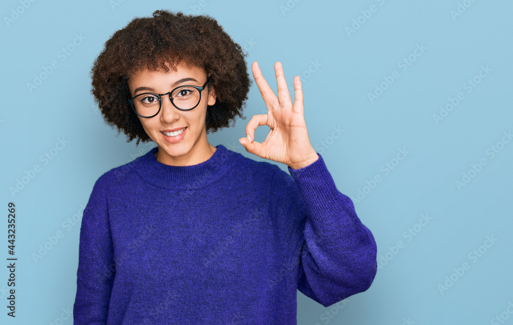 Young hispanic girl wearing casual winter sweater and glasses smiling positive doing ok sign with hand and fingers. successful expression. Young hispanic girl wearing casual winter sweater and glasses smiling positive doing ok sign with hand and fingers. successful expression.