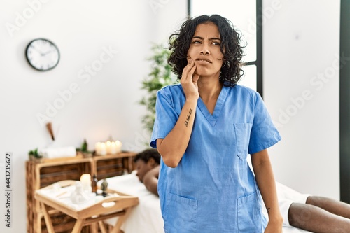 Young therapist woman at wellness spa center touching mouth with hand with painful expression because of toothache or dental illness on teeth. dentist