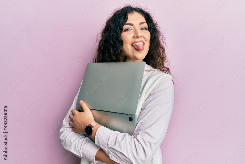 Young brunette woman with curly hair hugging laptop with love sticking tongue out happy with funny expression. Young brunette woman with curly hair hugging laptop with love sticking tongue out happy with funny expression.