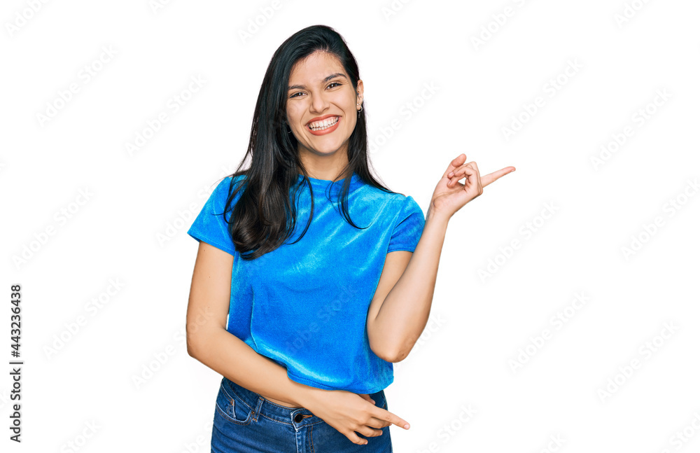 Young hispanic woman wearing casual clothes with a big smile on face, pointing with hand and finger to the side looking at the camera. Young hispanic woman wearing casual clothes with a big smile on face, pointing with hand and finger to the side looking at the camera.