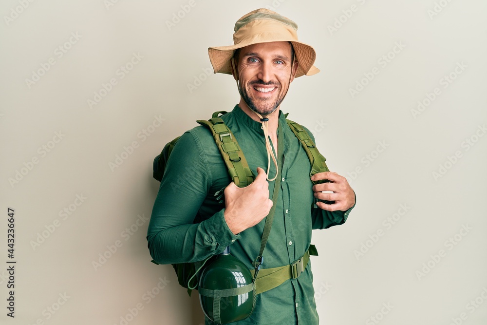 Handsome man with beard wearing explorer hat and backpack with a happy and cool smile on face. lucky person. Handsome man with beard wearing explorer hat and backpack with a happy and cool smile on face. lucky person.