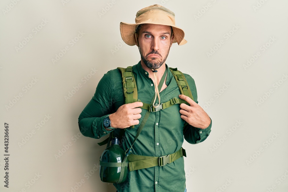 Fototapeta premium Handsome man with beard wearing explorer hat and backpack depressed and worry for distress, crying angry and afraid. sad expression.